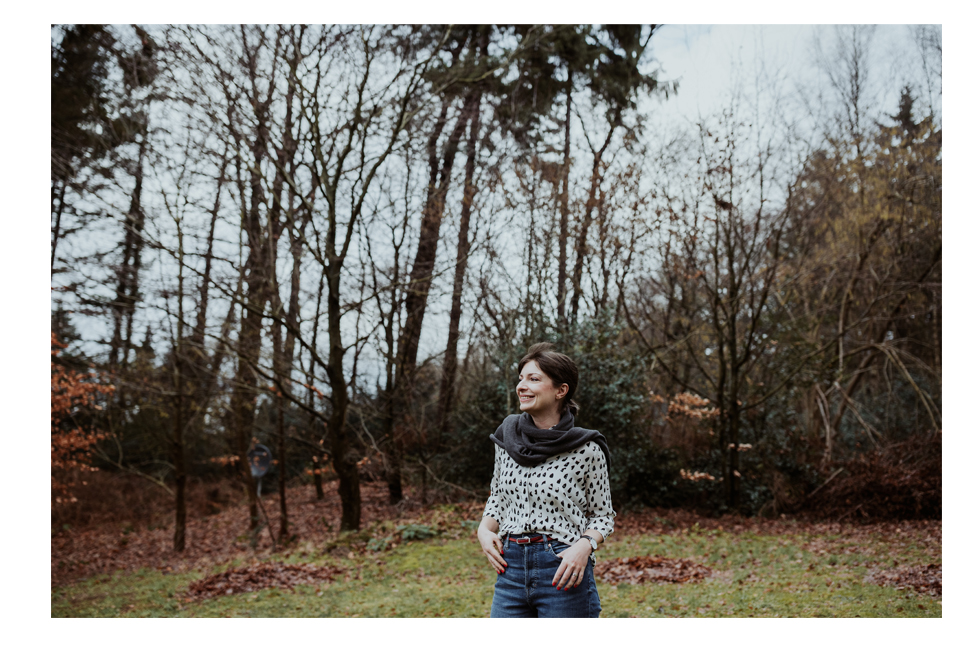Die Autorin Laura Newman steht lächelnd in einem Garten, umgeben von großen Bäumen